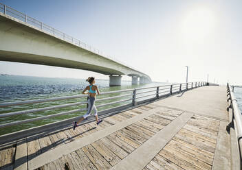 Rear view of woman jogging on bridge on sunny day - TETF01597