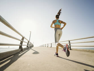 Rückansicht einer Frau beim Joggen auf einer Brücke an einem sonnigen Tag - TETF01598