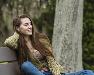 Smiling woman sitting on bench in park - TETF01603