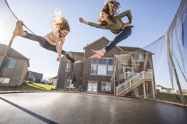 Girls (10-11, 12-13) jumping on trampoline in front of house - TETF01614