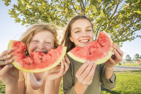 Porträt lächelnder Mädchen (10-11, 12-13) mit Wassermelonenscheiben im Garten - TETF01617