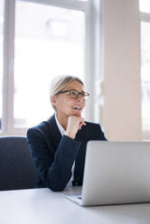 Lächelnde Geschäftsfrau mit Laptop am Schreibtisch im Büro - JOSEF08031