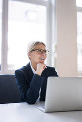 Smiling businesswoman with laptop at desk in office - JOSEF08031