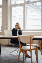 Businesswoman talking on smart phone at desk in office - JOSEF08042