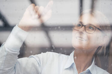 Businesswoman touching glass window at work place - JOSEF08043