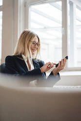 Geschäftsfrau, die im Büro eine Textnachricht auf einem Smartphone schreibt - JOSEF08044