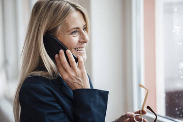 Lächelnde Geschäftsfrau im Gespräch auf dem Smartphone am Arbeitsplatz - JOSEF08047