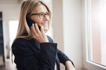 Lächelnde Geschäftsfrau, die im Büro mit einem Mobiltelefon spricht - JOSEF08048