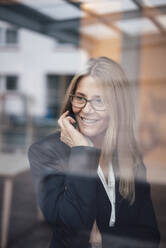 Lächelnde Geschäftsfrau durch Glas des Büros gesehen - JOSEF08050