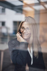 Smiling businesswoman seen through glass of office - JOSEF08050