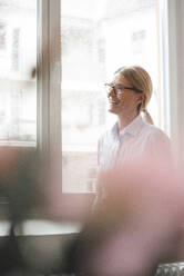 Cheerful businesswoman by window in office - JOSEF08072