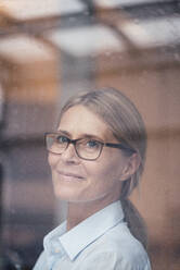 Mature woman with eyeglasses seen through glass - JOSEF08079