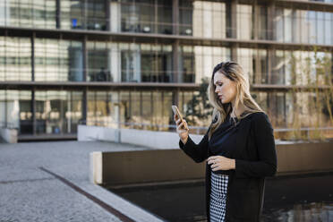 Geschäftsfrau mit Textnachrichten auf dem Smartphone vor einem Bürogebäude - DCRF01024