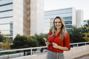 Smiling businesswoman with mobile phone in city - DCRF01044