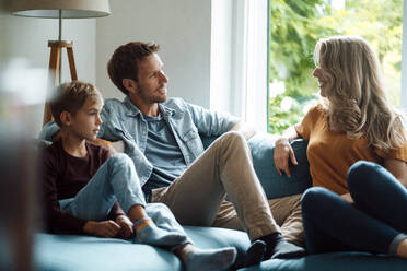 Man talking with woman sitting by son on sofa at home - JOSEF08080