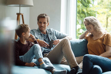 Son talking with mother and father sitting on sofa in living room - JOSEF08082