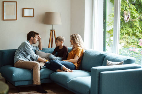 Mann und Frau sitzen mit ihrem Sohn auf dem Sofa im häuslichen Wohnzimmer - JOSEF08084