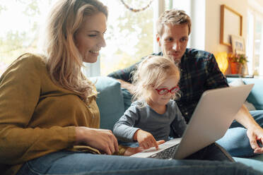 Little girl using laptop sitting with parents on sofa at home - JOSEF08085