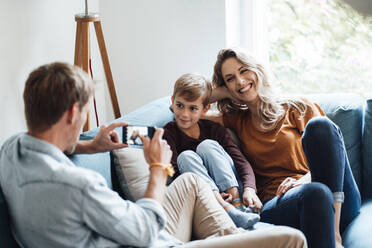 Man photographing son and cheerful woman through mobile phone at home - JOSEF08090