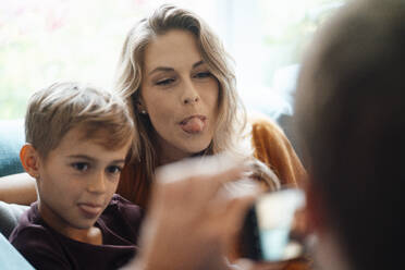 Blonde Frau mit Sohn, der die Zunge herausstreckt, wird von einem Mann zu Hause fotografiert - JOSEF08095