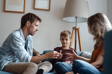 Eltern spielen Schere, Stein, Papier mit ihrem Sohn, der zu Hause auf dem Sofa sitzt - JOSEF08101