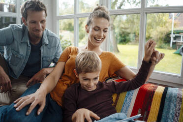 Happy mother and father sitting with son on sofa at home - JOSEF08102