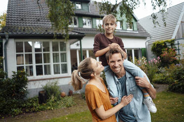 Lächelnder Mann trägt seinen Sohn auf den Schultern einer blonden Frau im Hinterhof - JOSEF08119