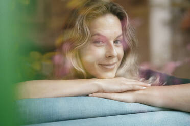Smiling beautiful blond woman leaning on sofa - JOSEF08125