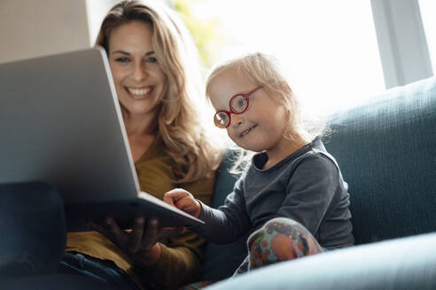 Kleines Mädchen mit Brille und Laptop bei der Mutter auf dem Sofa im Wohnzimmer sitzend - JOSEF08138