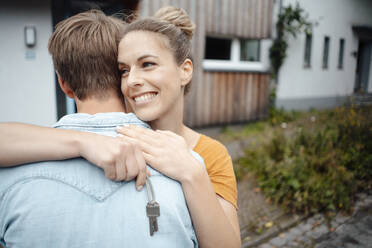 Happy blond woman holding house key hugging boyfriend at backyard - JOSEF08139