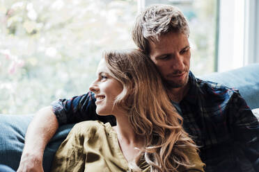 Smiling blond woman with boyfriend sitting on sofa at home - JOSEF08147