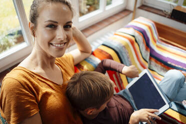 Lächelnde Mutter sitzt mit ihrem Sohn auf dem Sofa und benutzt einen Tablet-PC - JOSEF08160