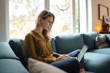 Blonde Frau mit Laptop auf dem Sofa im Wohnzimmer zu Hause - JOSEF08178