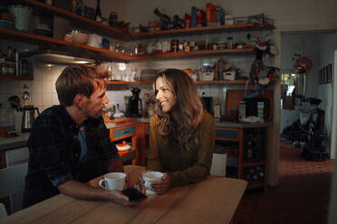 Lächelnde Frau im Gespräch mit ihrem Freund, der am Esstisch in der Küche sitzt - JOSEF08180