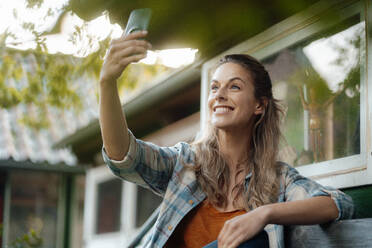 Happy woman taking selfie through mobile phone in backyard - JOSEF08199