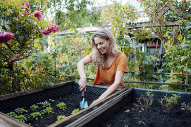 Lächelnde blonde Frau mit Schaufel bei der Gartenarbeit im Hinterhof - JOSEF08213