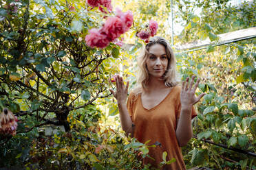 Blonde Frau steht inmitten von Pflanzen im Hinterhof - JOSEF08214