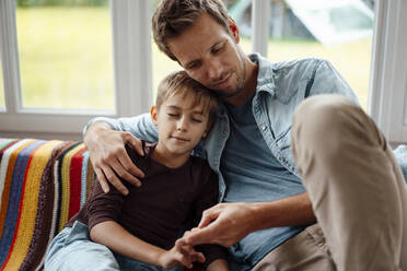 Father sitting by son with eyes closed on sofa at home - JOSEF08250