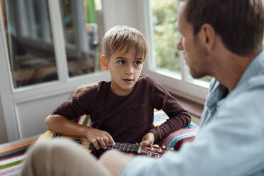 Blond boy with guitar talking with father at home - JOSEF08254