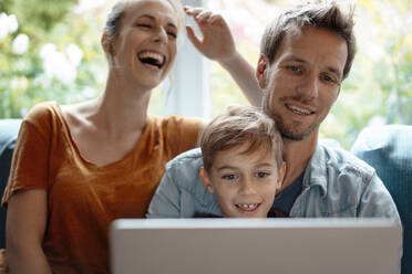 Cheerful woman sitting by man and son sharing laptop at home - JOSEF08261