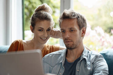 Smiling woman sitting by boyfriend using laptop at home - JOSEF08262