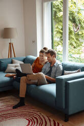 Glückliches Paar mit gemeinsamem Laptop auf dem Sofa im Wohnzimmer zu Hause - JOSEF08263