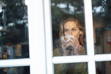 Blonde Frau trinkt Kaffee durch ein Glasfenster gesehen - JOSEF08273