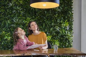 Smiling mother with daughter turning on pendant light with tablet PC at home - DIGF17756