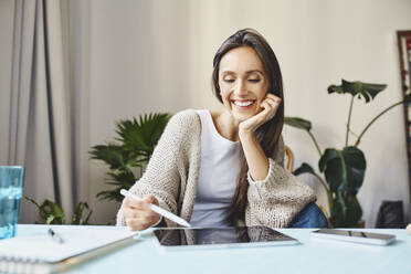 Glückliche Frau, die am Schreibtisch sitzend ein digitales Tablet mit digitalisiertem Stift benutzt - BSZF02007