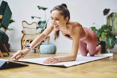 Happy woman touching tablet PC on exercise mat at home - BSZF02034