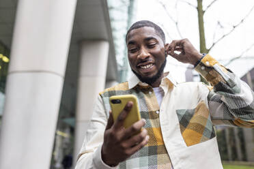 Smiling man wearing wireless in-ear headphones having video call on mobile phone - WPEF05858