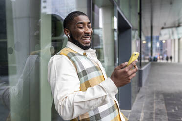 Glücklicher Mann surft mit seinem Smartphone vor einer Glaswand im Internet - WPEF05872