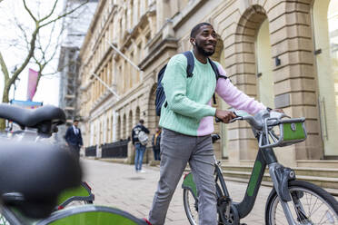 Smiling man with electric bicycle walking on footpath - WPEF05888