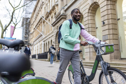 Lächelnder Mann mit Elektrofahrrad auf dem Gehweg - WPEF05888